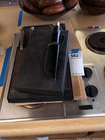 Photo of hunting knife in black leather sheath on top of various cutting boards and wooden bowls in background