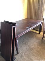 Photo of the dining table set with two additional leaves detached and placed to the side, showing side view of table legs and leaves