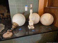 Two vintage white globe hanging lamps with brass fittings, one white ceramic table lamp base, and two white glass globe shades on a black surface.