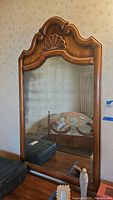 Front view of vintage wood framed mirror showing carved top detail, wood grain, and reflective glass.