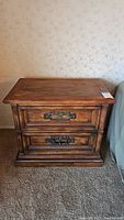 Front view of wooden nightstand showing two drawers with ornate metal handles and worn wood finish