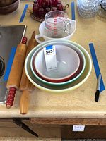 Set of 4 Pyrex mixing bowls nested together along with 2 wooden rolling pins and 2 Pyrex measuring cups on a table.