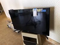 Samsung TV front view showing the full screen and stand on a small white cabinet.
