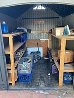 Full interior view of shed with two wooden shelving units holding assorted shed contents including milk crates, boxes, and containers.