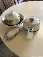 Three stoneware items displayed together: two bowls (one with floral pattern) and a covered dish with a round brown knob lid and handle, plus rectangular butter dish tray with lid.