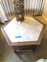 Front angled view of the vintage wooden hexagon coffee table showing the marble top and some of the wooden frame and base shelf.