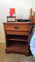 Wood nightstand shown from the front, with items placed on top and the drawer closed.