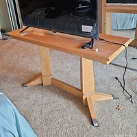 Front view showing the full wood side table supporting a flat screen TV with visible rectangular wood top and central pedestal base with splayed legs and metal caps.
