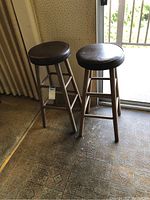 Two wooden bar stools with vinyl seats placed on patterned floor near sliding glass door.