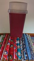 Photo showing the red Sterilite container on top of multiple rolls of Christmas-themed wrapping paper with snowman and Santa Claus prints.