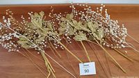 27 decorative branches with gold leaves and pearl-like silver bead clusters laid out on a wooden floor.