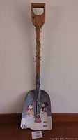 Full view of the shovel showing wooden handle and painted metal blade with snowman scene.