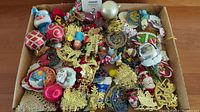 Top view of box containing assorted vintage Christmas ornaments including glass baubles, fabric figurines, and metal decorations
