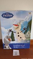 Front view of boxed Disney Frozen Lighted Olaf yard decor, showing Olaf figure and Frozen branding with 28 inch size description.