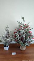 Pair of two flocked faux Christmas trees on wooden surface, showing size difference and overall look