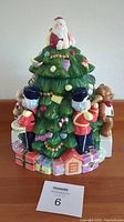 Front view of ceramic Christmas tree cookie jar showing Santa on top and toys around the base.