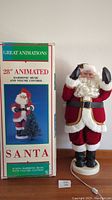 Front view of the Santa Claus figure standing next to the original box, showing the full height and colorful outfit.