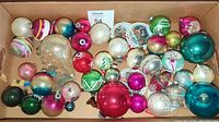 Top view of box containing a variety of vintage blown glass Christmas ornaments in different colors and shapes.