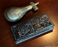Brass powder horn alongside metal trinket box with relief design lid