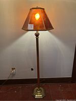 Full view of the lamp turned on, showing the amber-brown mica shade illuminated and cast warm light on the wall.