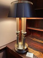 Full view of the classic three pillar lamp with black shade on a wooden surface, highlighting the chrome and brass materials and overall design.