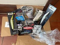 Fishing accessories box with reels, fishing line, plastic baits, and lures in packaging and loose inside an open box.