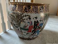 Side view showing the geisha figures in traditional dress and floral accents on the jardiniere's exterior.