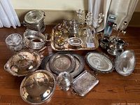 Full view of all silver plated serving items laid on floor with variety of trays, bowls, teapot, and candelabra