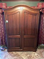 Front view of the large solid wood wardrobe with double paneled doors and curved cornice top, showing brass handles.