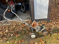 Full side view of the entire Stihl gas-powered tiller showing engine, handlebar and wheels