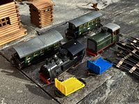 Close-up of two vintage Biller Bahn wind-up model train engines in black and green, two green passenger cars, yellow and blue small plastic containers, and several curved wooden track pieces.