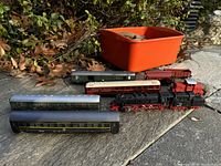Lot of vintage Fleischmann model train engines, cars, track and more, placed outdoors on stone surface with a red container holding track pieces.