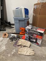 Full lot overview showing the Peak jump starter box, saws, work gloves, tote bins, and red flashlight on concrete floor.