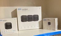Three sealed Blink security camera kits side by side: 3-camera Outdoor kit, single Outdoor kit, and Mini kit