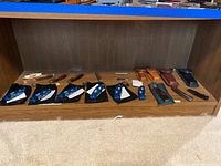 Full view of lot items on wood shelf: eight blue folding box cutters with black velvet pouches, four leather sheaths in different colors, and one metal wrench.
