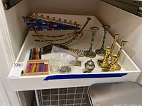 Overview of two menorahs, candlesticks, drip catchers, spice box and candles on white tray