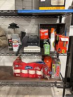 Photo of black metal shelf holding assorted household and cleaning supplies, trash bags, toilet paper, paint spray can, and Coleman lantern on top and middle shelf.