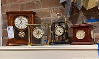 Set of four clocks displayed together on a shelf against brick wall.