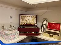 Photo showing four jewelry boxes and displayed costume jewelry including gold-tone necklaces and bracelets on a shelf.