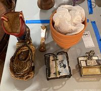 Photo showing large decorative cowboy boot planter with attached rope and metal belt, multiples stacked plain terracotta pots, metal decorative book, bottle opener and small brass trophy.