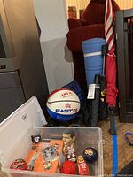 Photo shows basketball, blue yoga mat, umbrellas, bobbleheads, ornaments, and basketball cards inside a plastic storage bin.