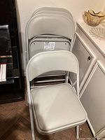 Four grey folding chairs stacked, showing vinyl seats and metal frames.