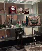 Wide view of golf collectibles including clocks, metal figurines, and decorative pillow displayed on glass shelves above a sink.