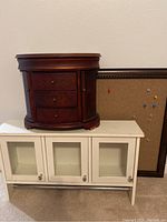 Wooden jewelry case on top of white wall shelf with cork board behind them
