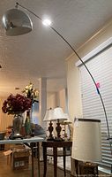 Silver-colored arc floor lamp with dome-shaped shade in a room with other furniture and lamps.