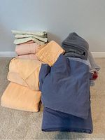 Photo showing folded bed linens and towels in various colors stacked on the floor