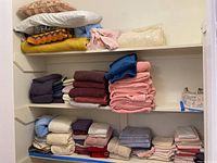 Shelves filled with folded bed linens including sheets, pillowcases, blankets, and pillows in various colors and patterns.