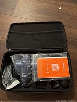 Open case showing the massage gun, USB charging cable, instruction manual, and four massage attachments individually packed in plastic.