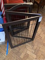 Full view of the bronze-colored metal folding gate folded and standing on the floor showing overall size and structure.