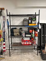 Front view of black metal wire shelving unit holding various household and garage items such as paper towels, canned goods, and camping equipment.